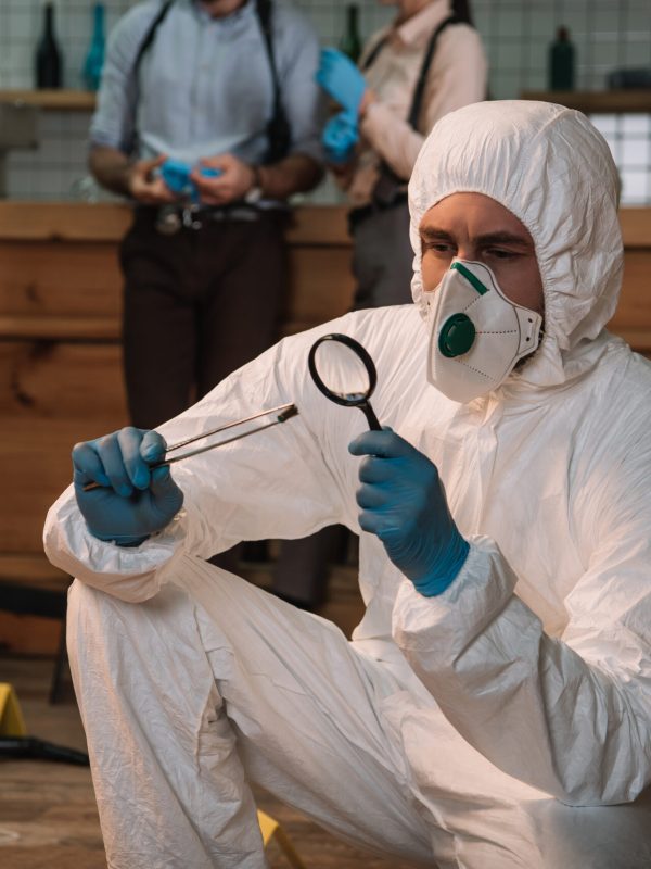 focused forensic investigator examining evidence with magnifying glass at crime scene with